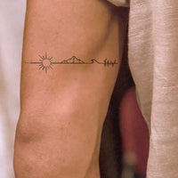 Long line tattoo with sun, mountain and sea.